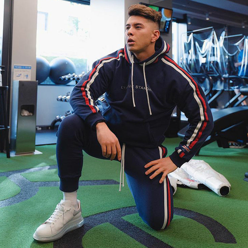 Sports fitness pullover in navy blue with red and white striped sleeves, worn by a model in a gym setting. Cotton material, available in sizes S-3XL.