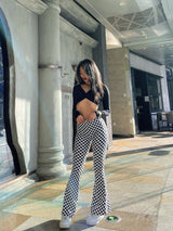 Trendy plaid yoga bell-bottoms in a black and white chessboard pattern, worn by a model in an urban outdoor setting. Great for fitness and casual wear.