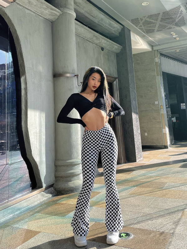 Model wearing chessboard plaid yoga bell-bottoms paired with a black crop top. These high-waisted plaid yoga pants offer a trendy and flexible fit.